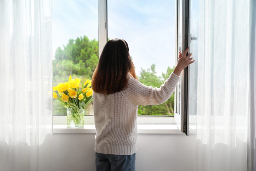 woman opening and looking out her window next to a vase of tulips